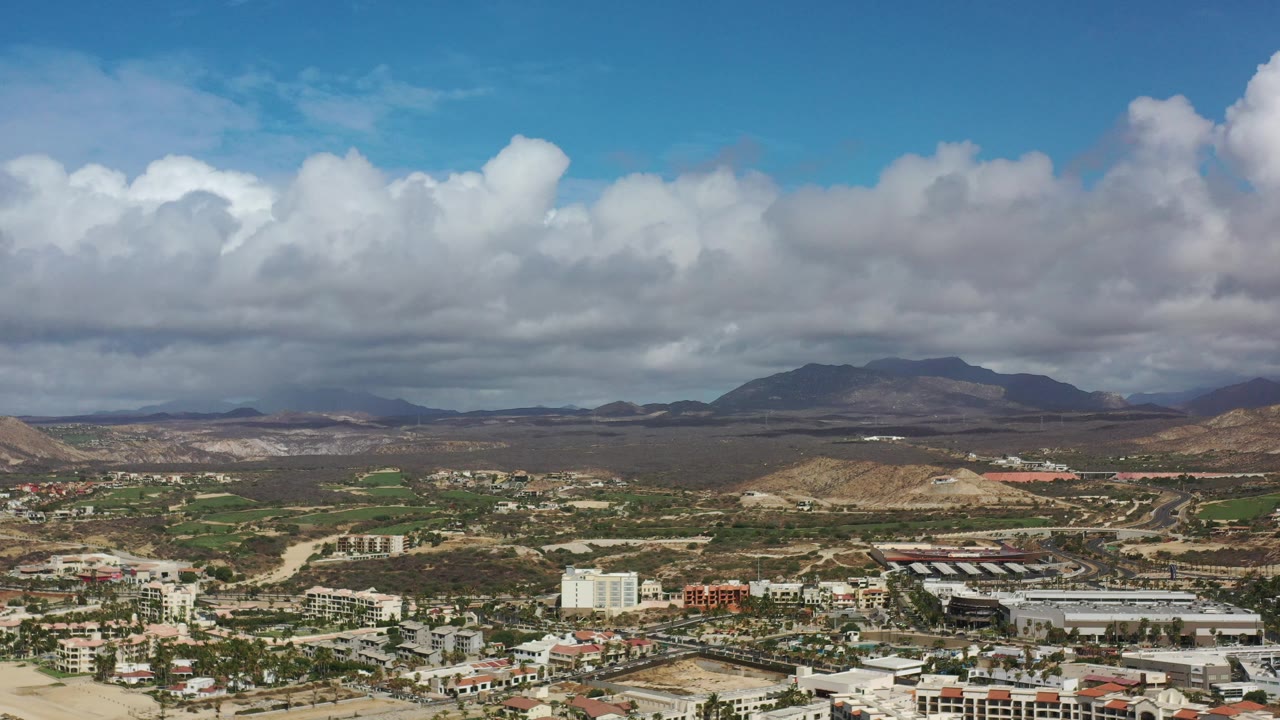 Town and desert hills seen from above under a bright cloudy sky.