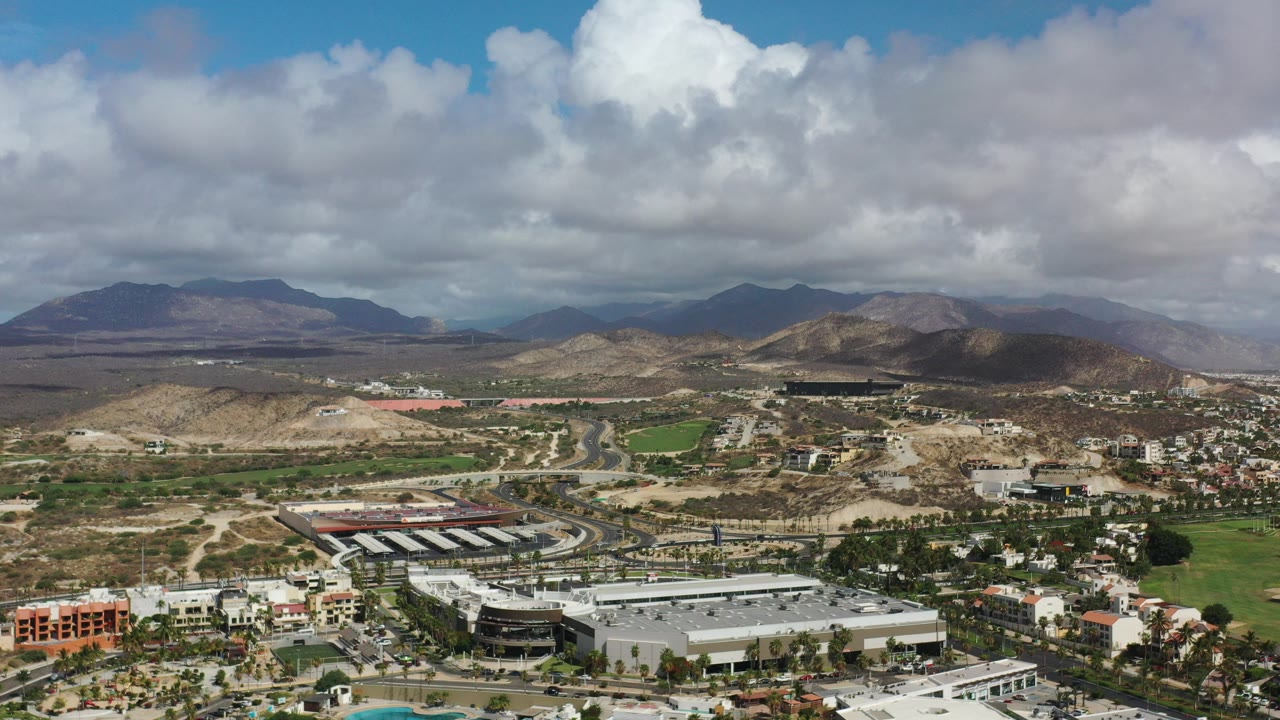 Aerial view of a town, roads, dry hills, mountains, and large clouds.