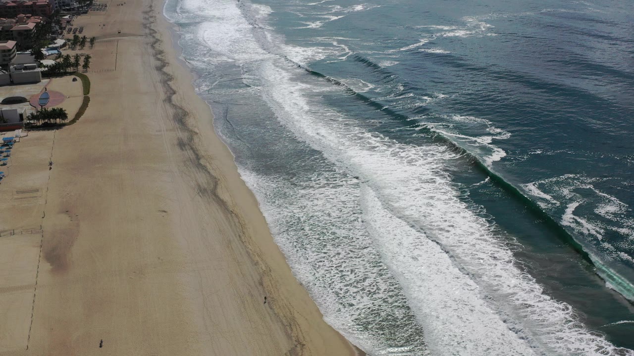 Aerial view of surf rolling along a sandy beach.