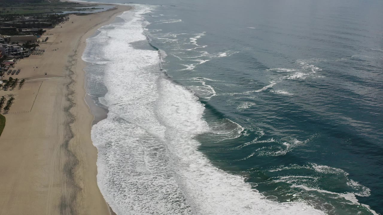 Oblique aerial view of surf lines curling beside a long beach.