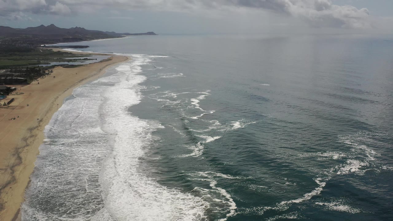 Aerial beach and ocean view with whitewater surf and hazy horizon.