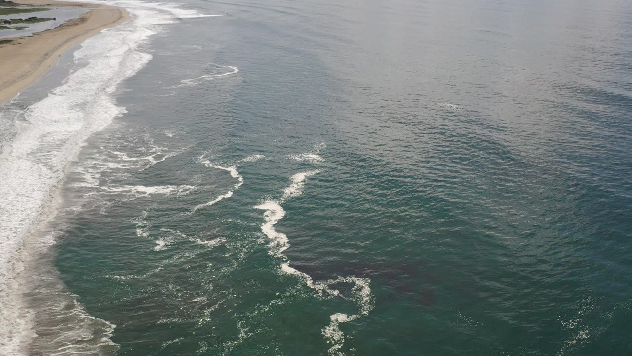 Aerial view of surf meeting a sandy beach.