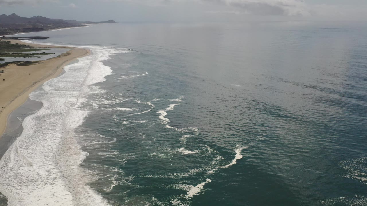 Diagonal beach shoreline with white waves and a broad ocean surface.