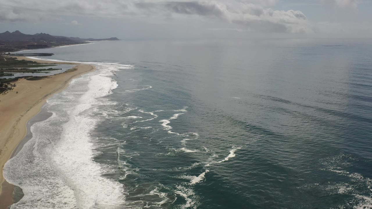 Ocean shoreline with foamy waves and a hazy mountain horizon.