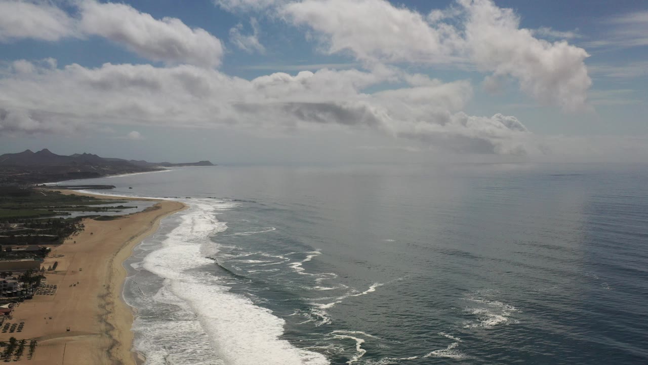 Aerial view of waves breaking along a sandy beach under clouds.