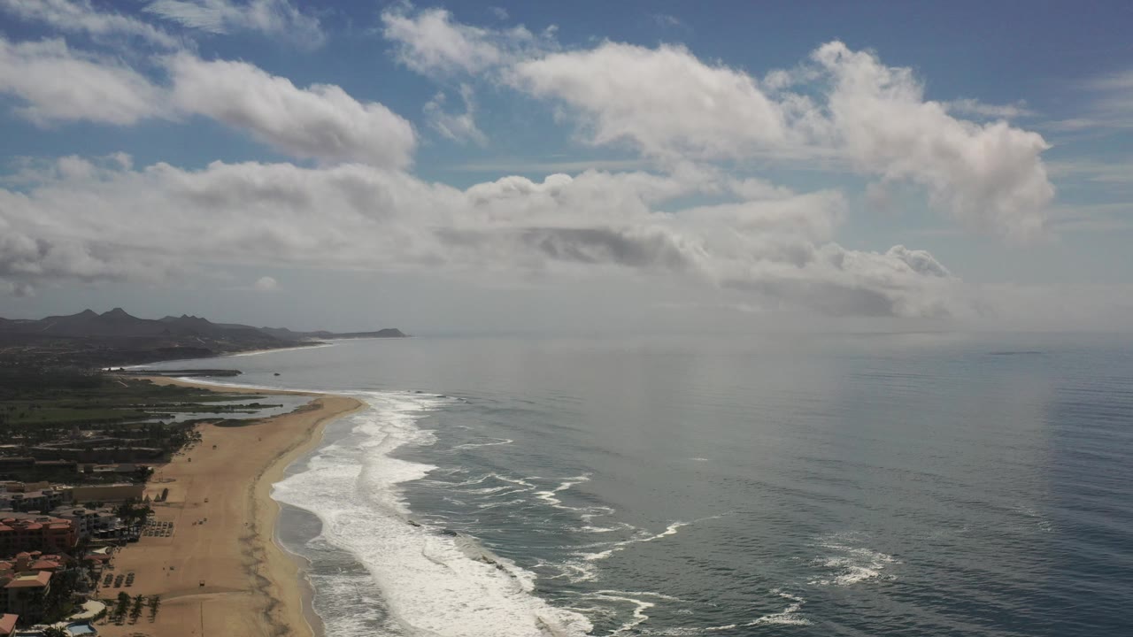Aerial coastline with bright surf lines and hazy ocean horizon.