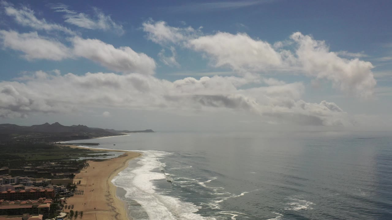 Coastal aerial view with beach, ocean, hills, and large clouds over Los Cabos.