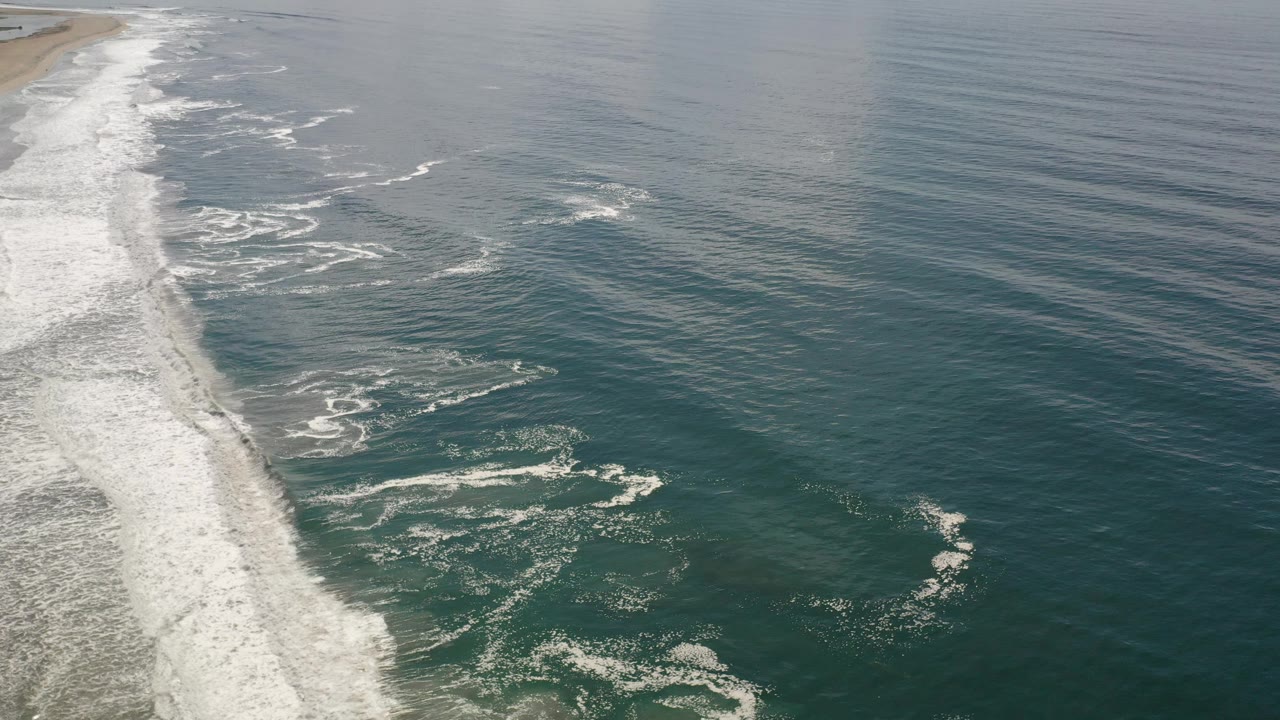 Coastline surf and calm blue-green water from above.