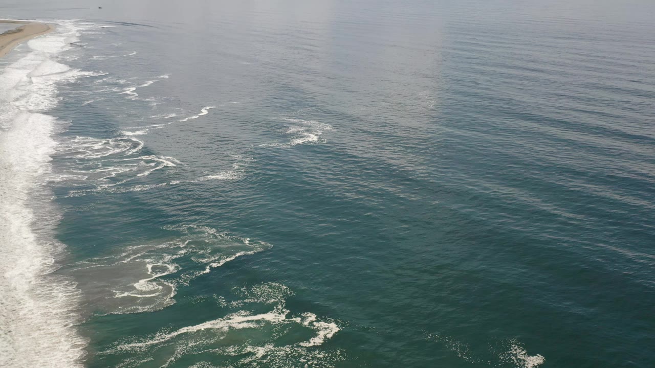 Los Cabos ocean surface with foamy wave trails near the left side and broad open water extending to the right, no visible people.