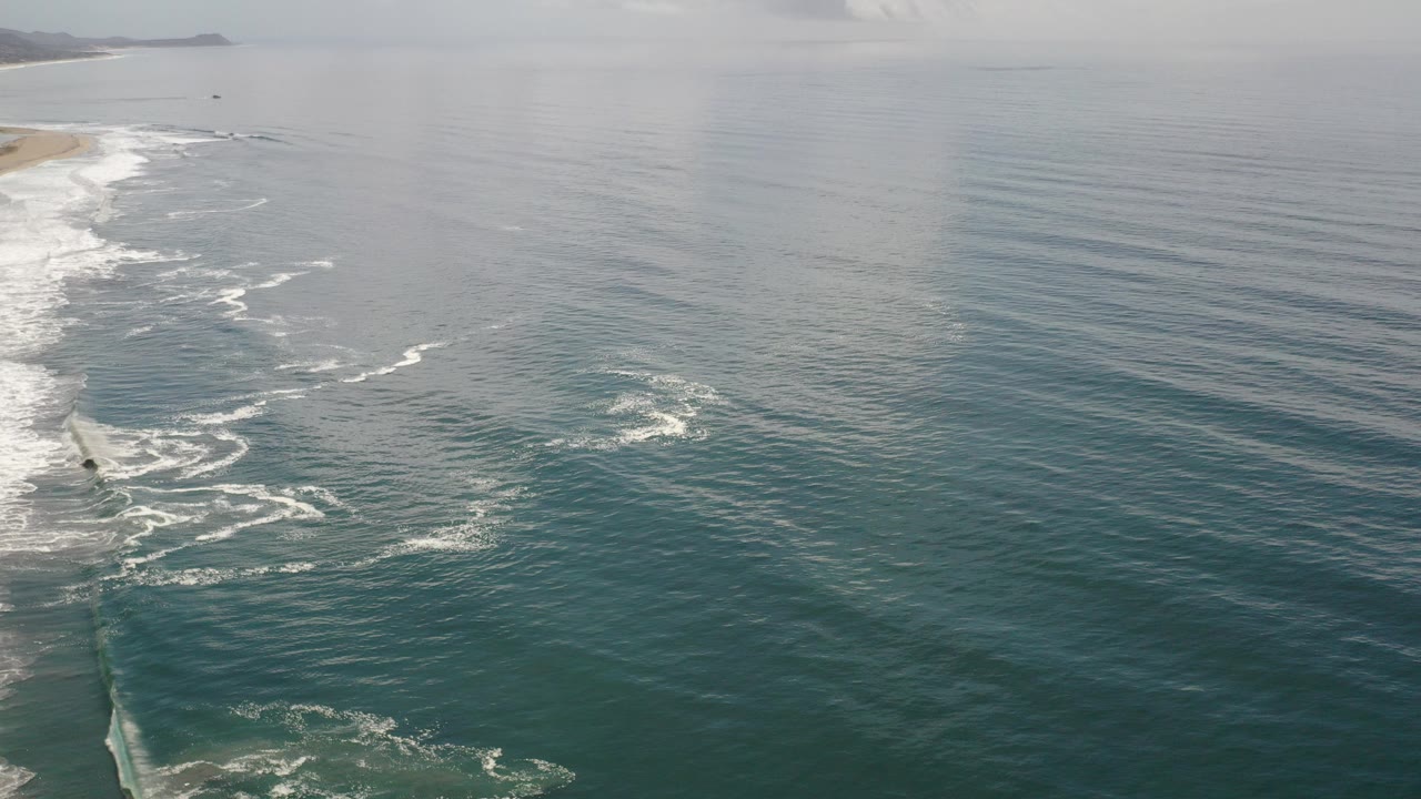 Aerial view of blue ocean beside a surf-lined shoreline.