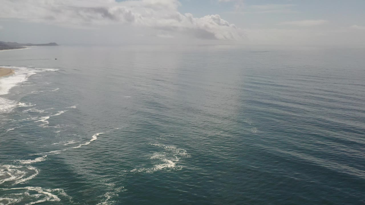 Open ocean with parallel swell lines and beach at left.