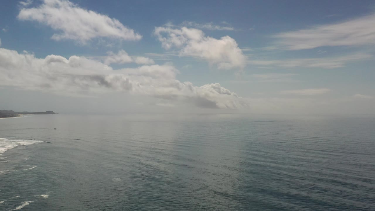 Wide ocean horizon with clouds and faint coastline on the left.