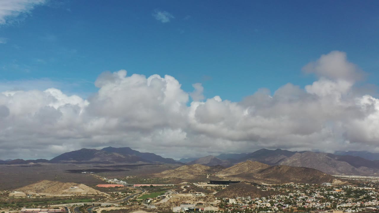 Wide aerial landscape with clouds, hills, and roads