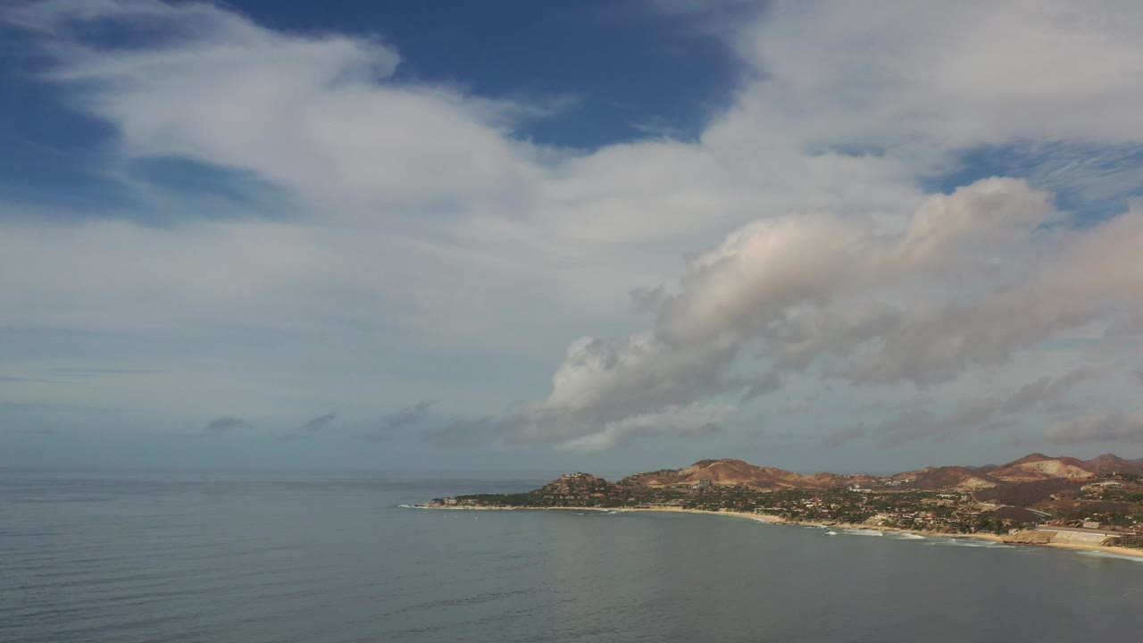Calm sea beside a developed shoreline under large white clouds.
