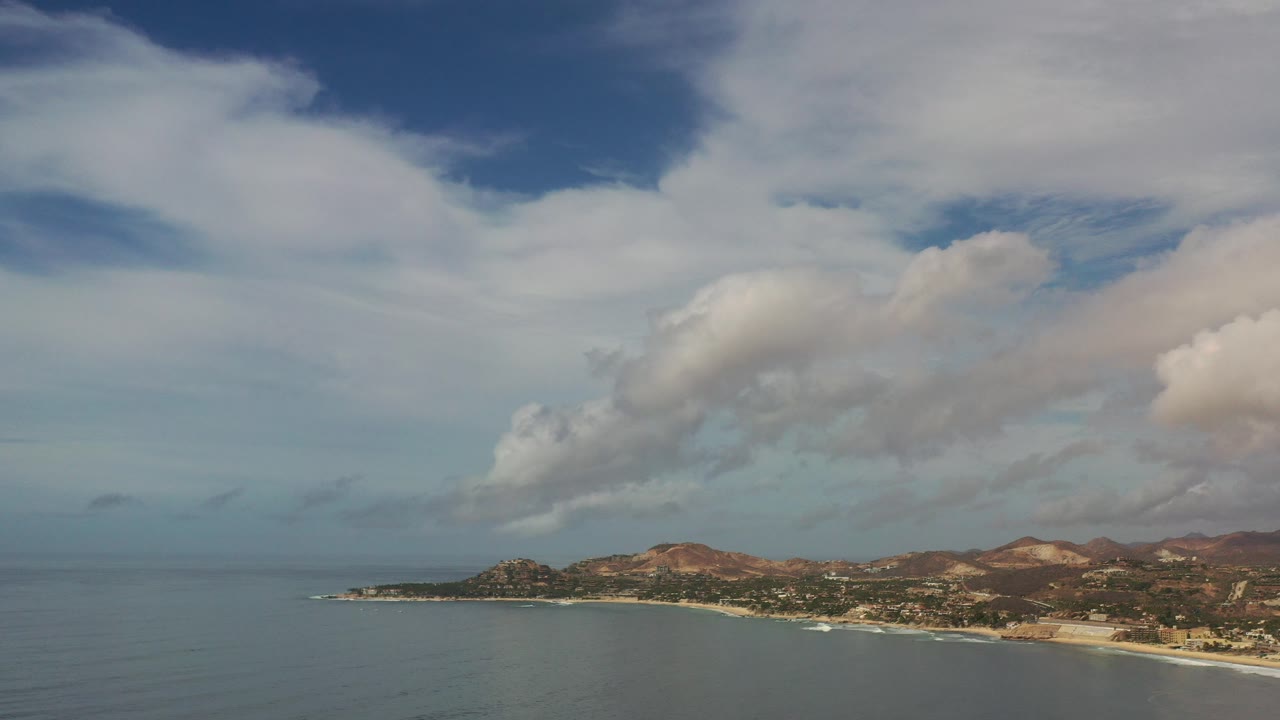 Wide aerial view of ocean, beach, hills, and clouds.