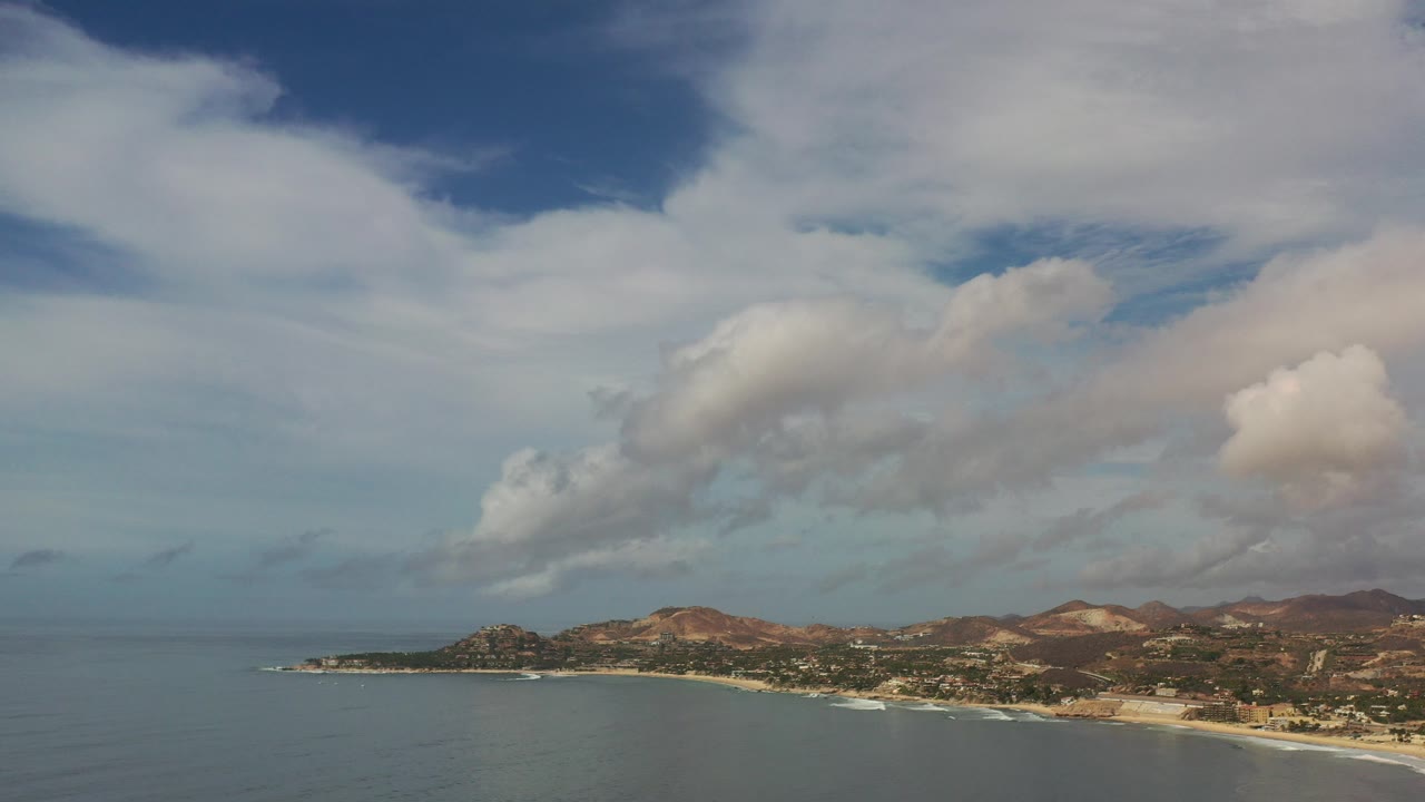 Clouds over ocean, beach, and low coastal hills.