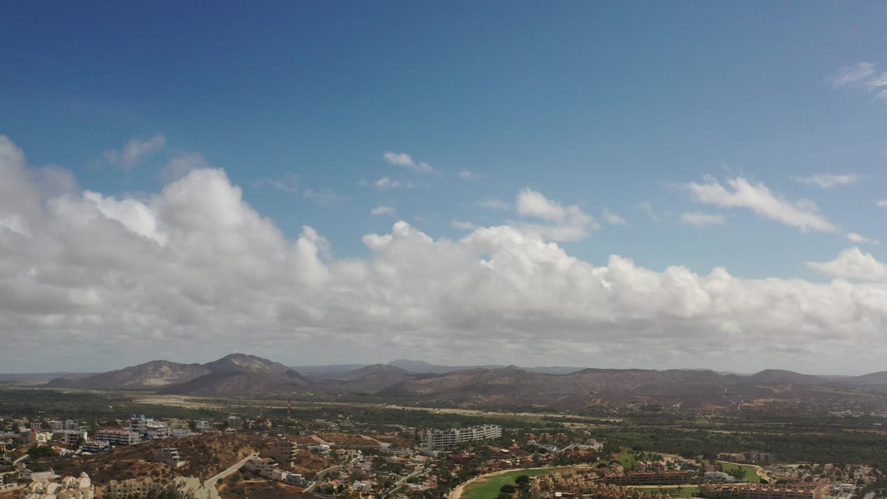 Wide aerial view of a valley town beneath clouds and distant mountains.
