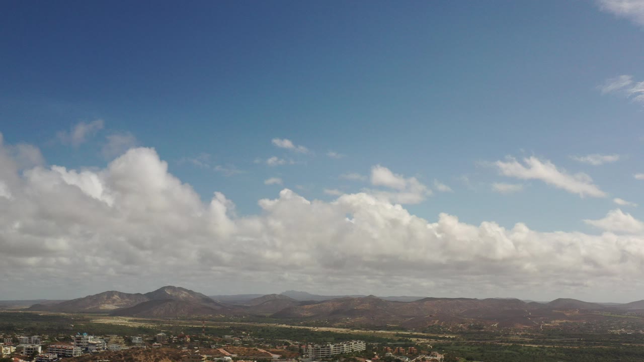 Cloudy sky above low mountains and distant town edge.