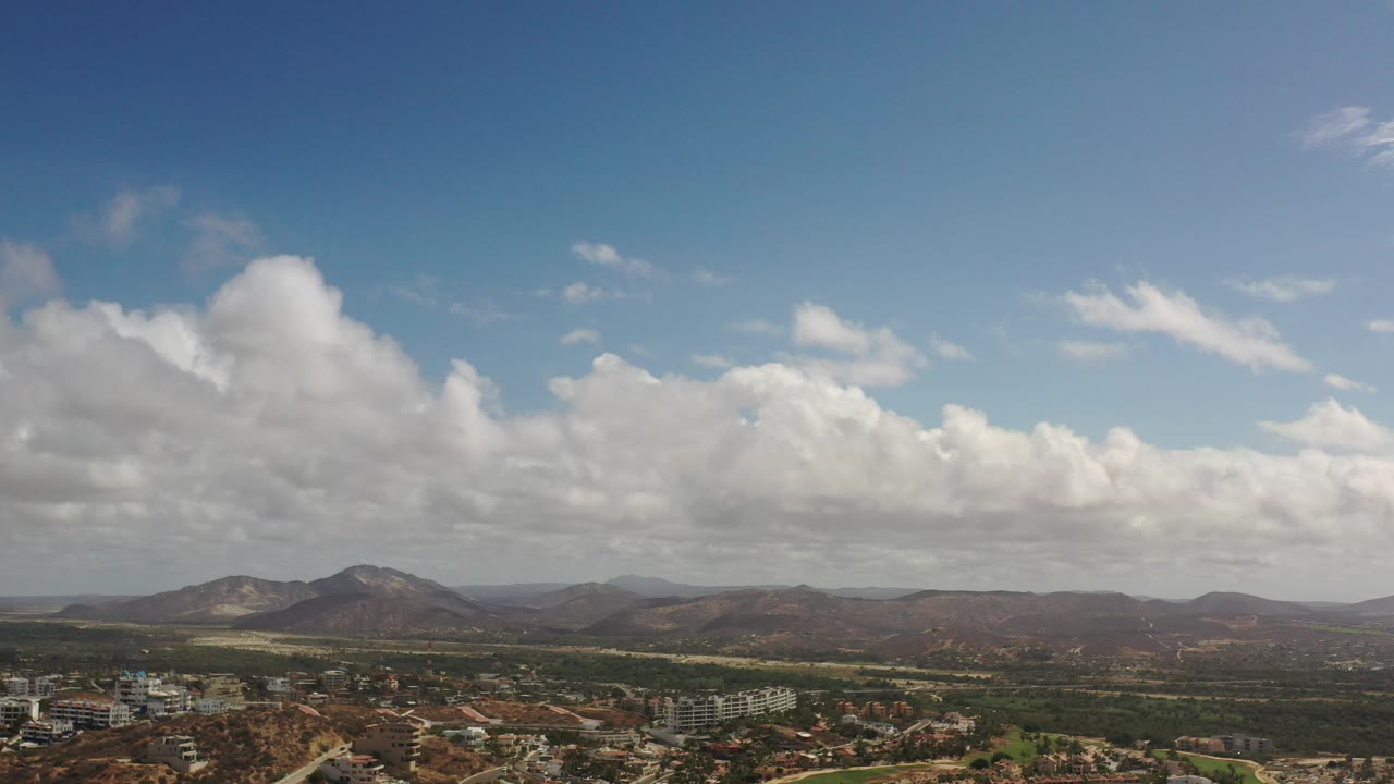 Elevated view across buildings, green land, distant hills, and clouds.