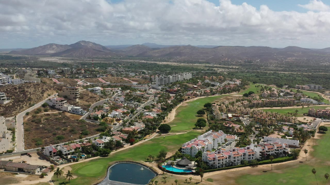 Drone view of residential streets, green fairways, desert hills, and mountain ridge.