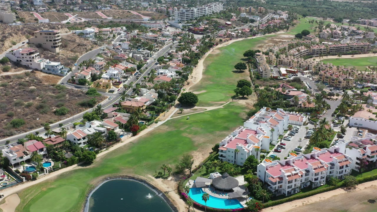 High view of golf green, pond edge, swimming pool, roads, and resort apartments.