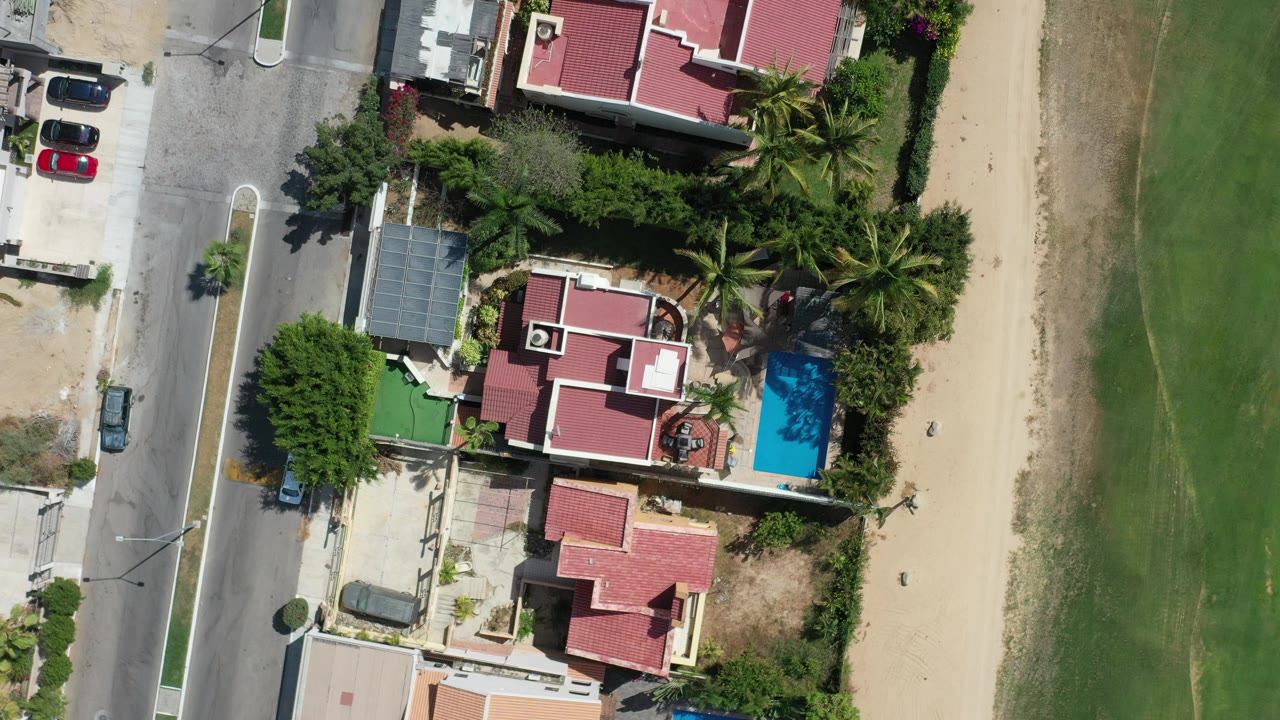 Overhead view of homes, palms, road, pool, sand, and green space.