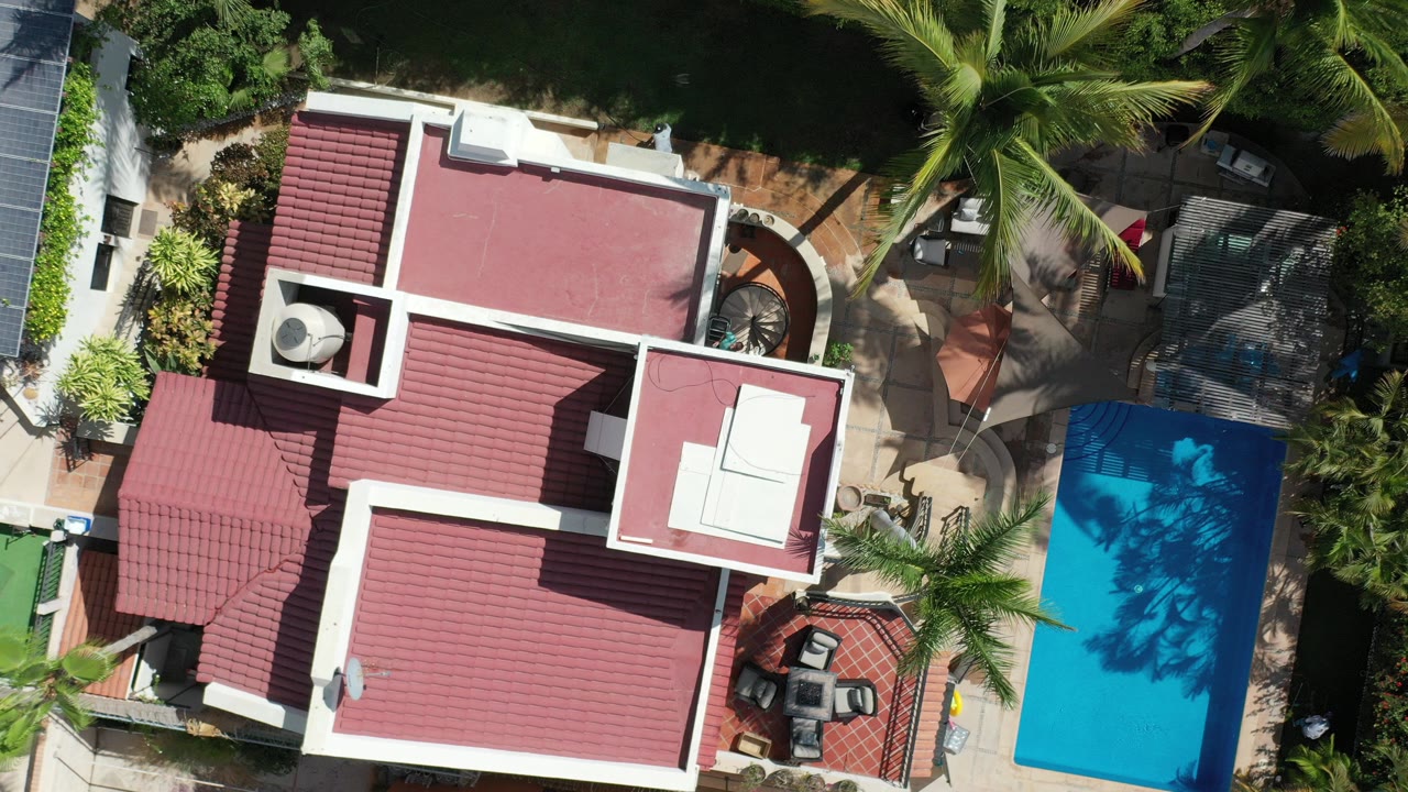 Top-down view of red-roofed home, pool, palms, and patio.