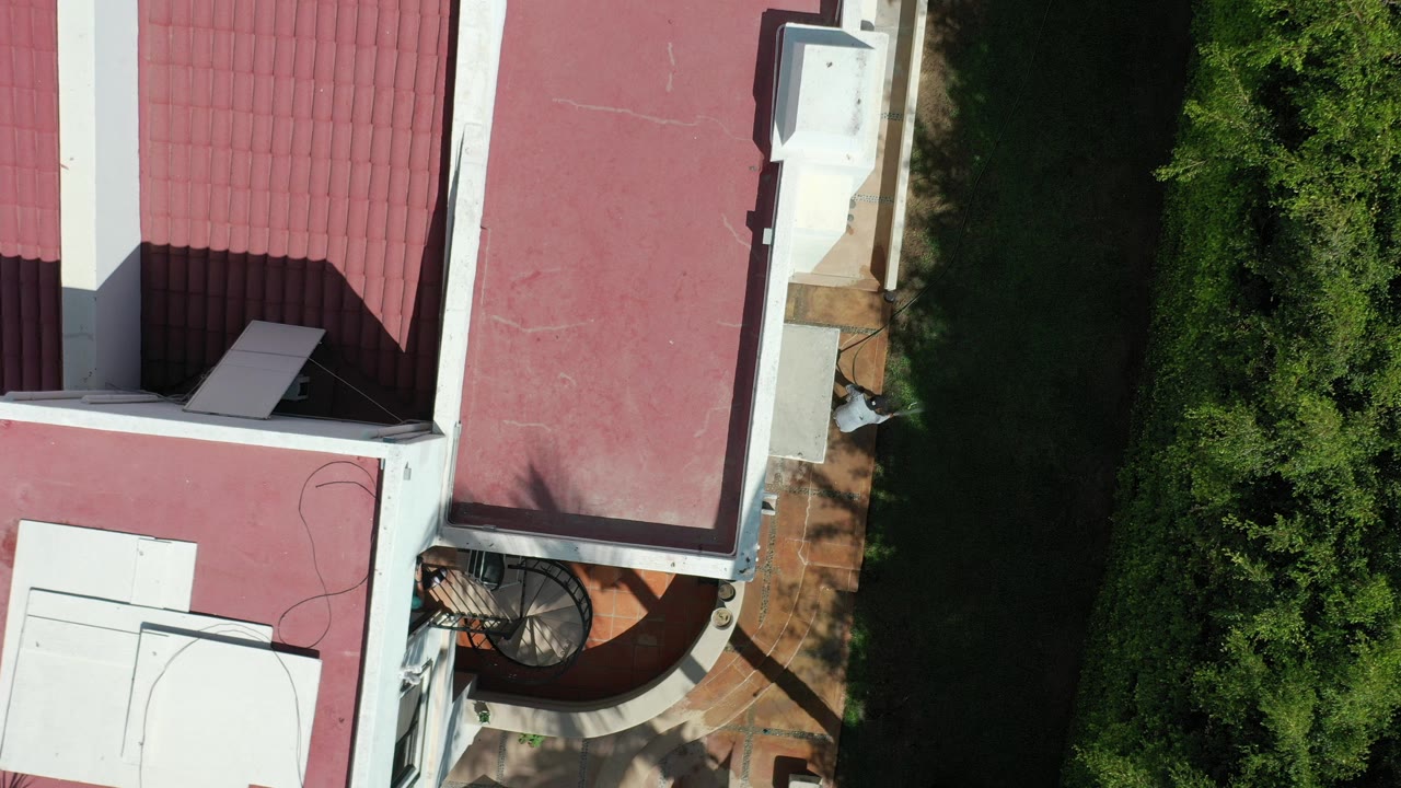 Overhead view of a red-roofed house, balcony, grass strip, and hedge.