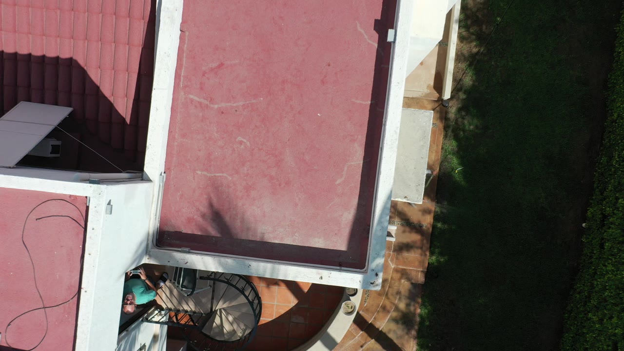 Overhead view of a red roof, white walls, lawn, patio, and spiral stair.