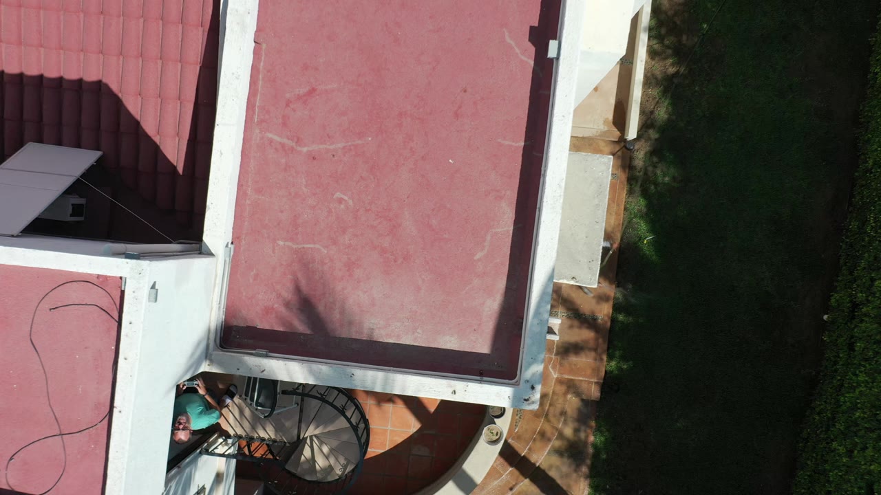 Overhead Los Cabos frame with the red roof centered, white roof borders, a shaded green lawn on the right, and the spiral stair area partly visible at the bottom.