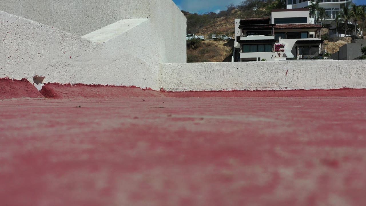 Red floor beside short white stucco walls with buildings beyond.