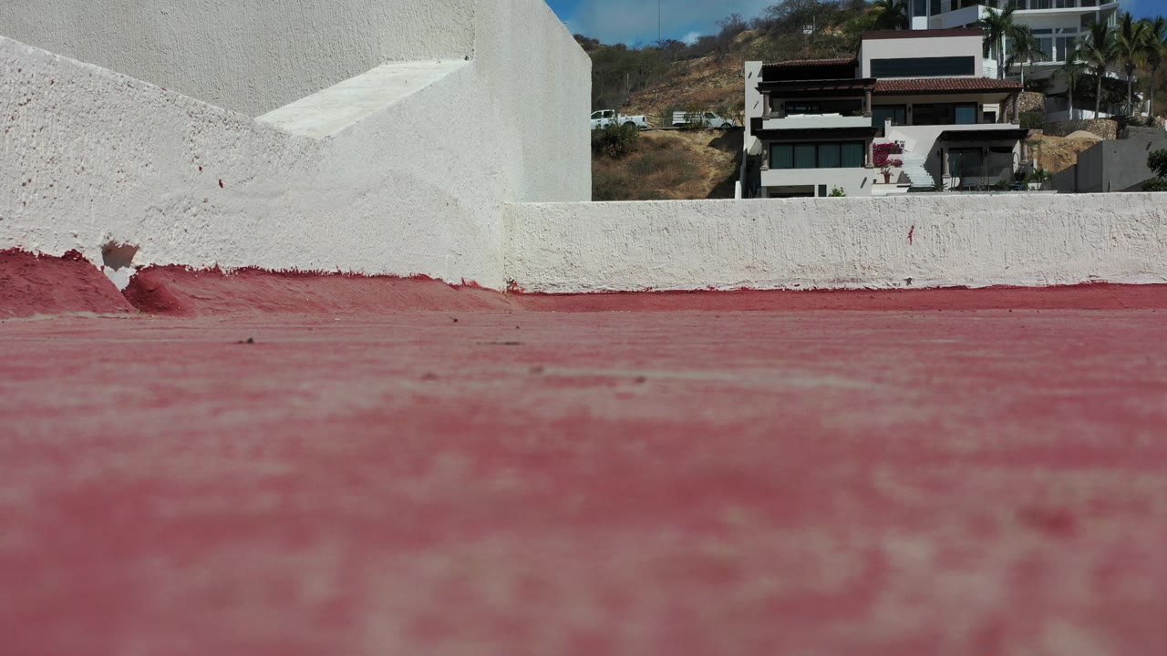 Low view of a red terrace floor and white stucco wall with homes in the background.