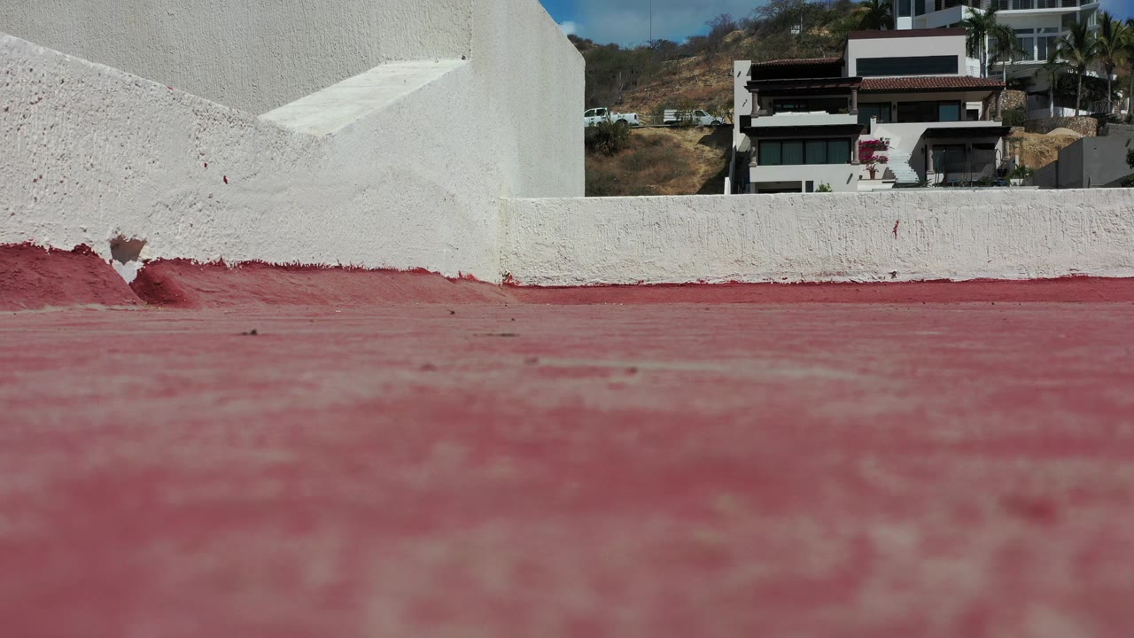 One second in, the red foreground remains soft while the white wall and distant Los Cabos houses sit sharply near the top of the frame with no visible people.