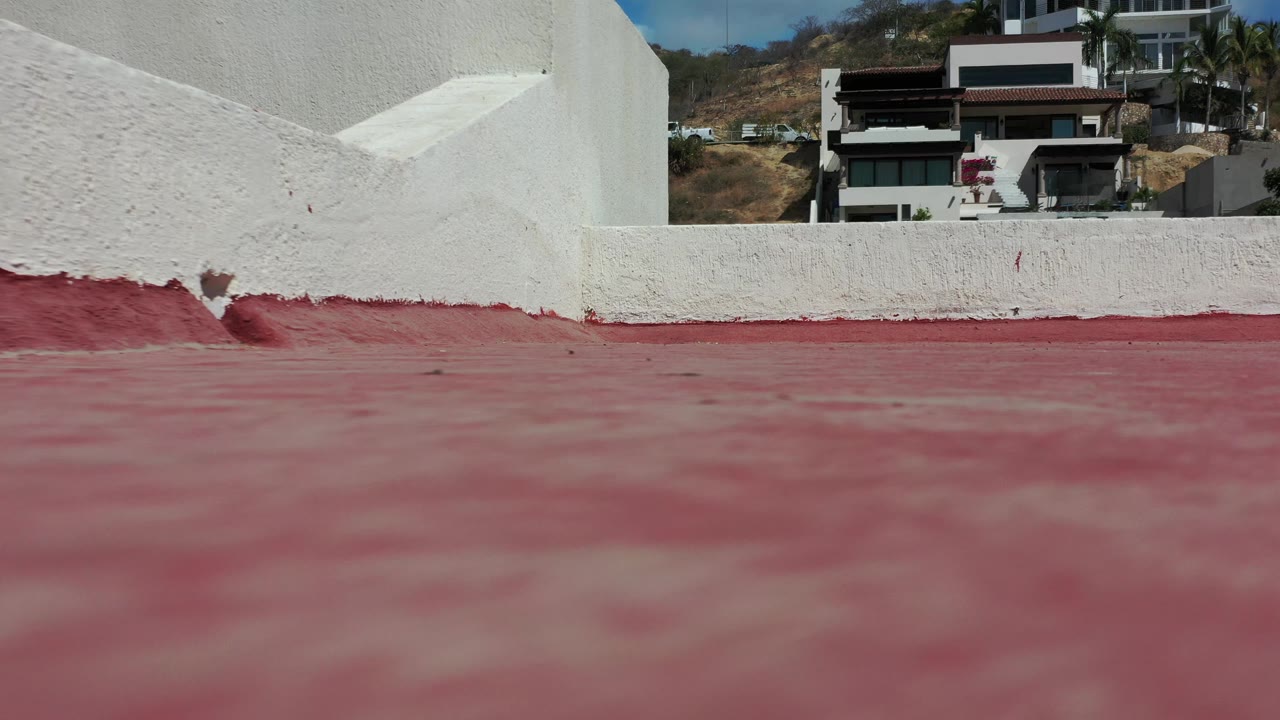 Los Cabos rooftop frame with a white parapet crossing the foreground, a red roof below, distant residential buildings, and no visible people.