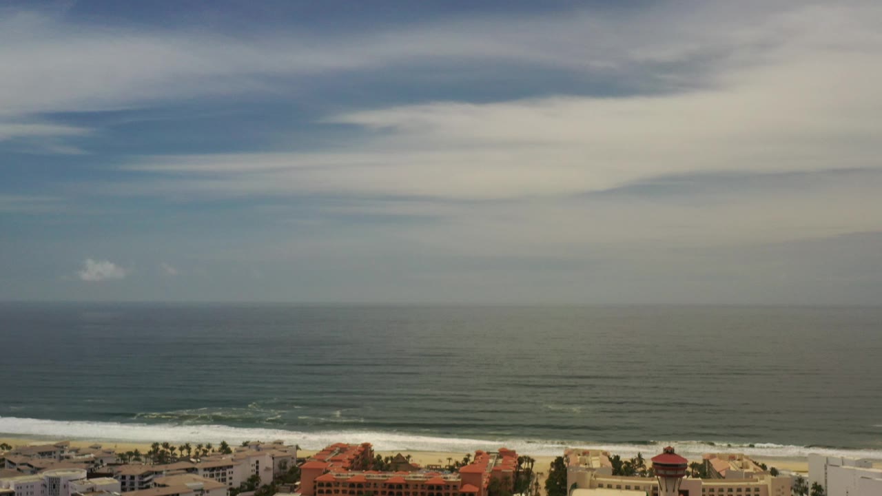 Ocean, surf, and shoreline buildings below clouded sky.