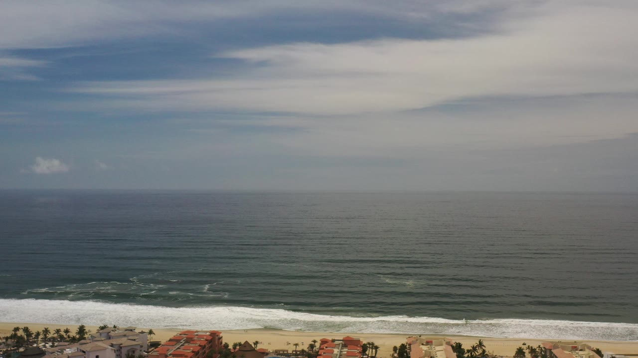 Wide ocean horizon with cloudy sky and surf below.