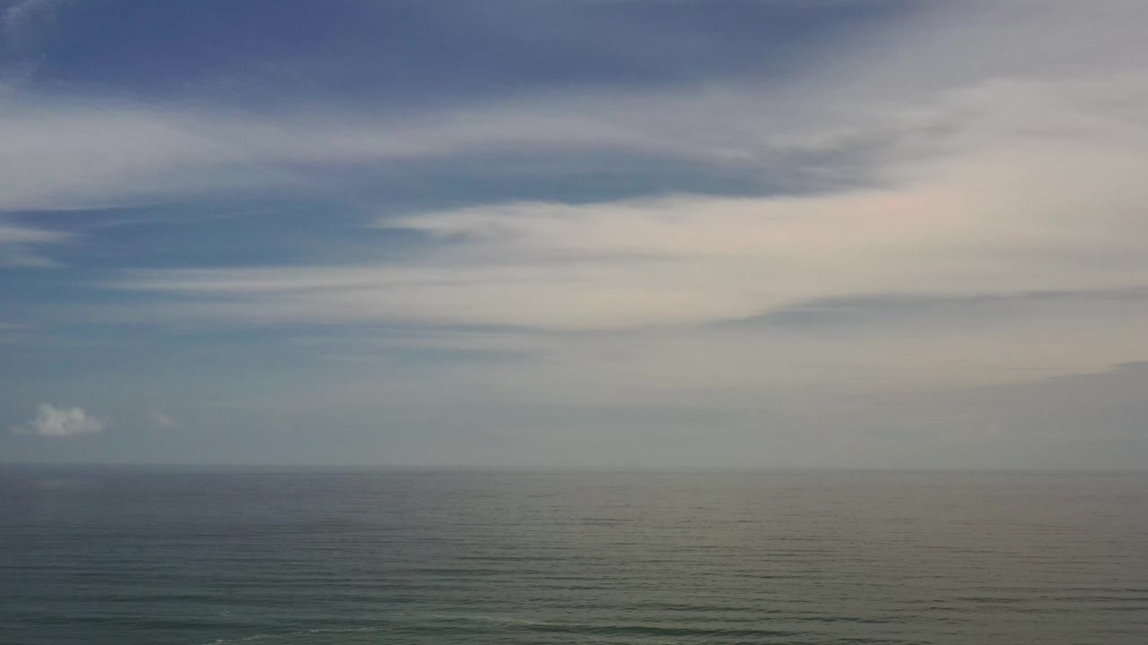 The ocean fills the lower portion of the Los Cabos frame while a broad, pale cloud band stretches across the sky, with no visible people.