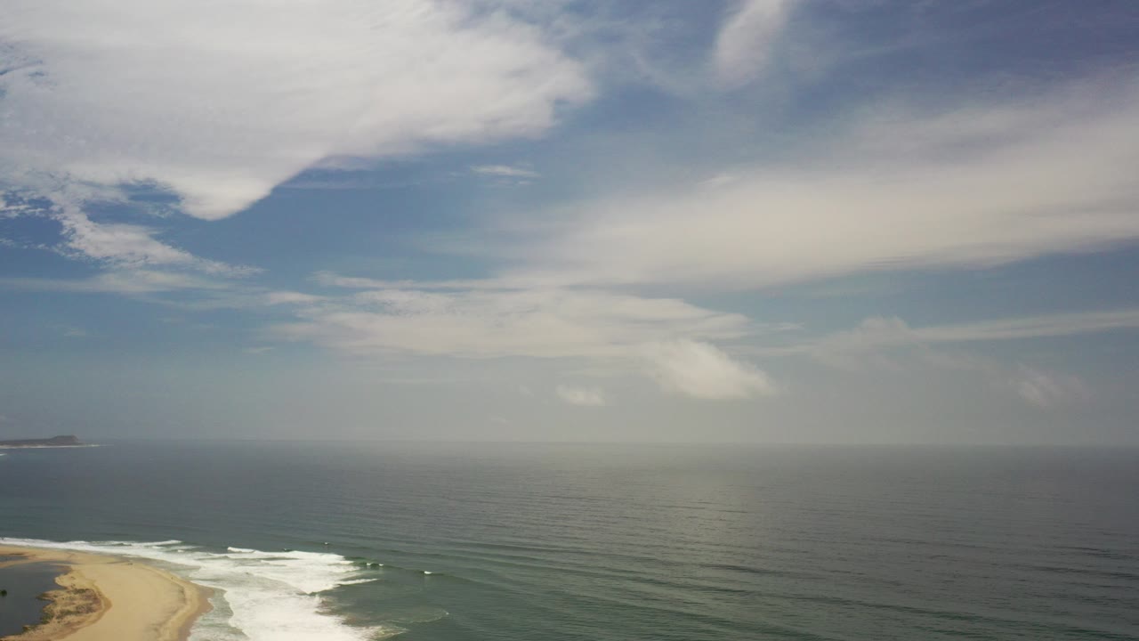 Elevated view of surf meeting a sandy beach under a clouded sky.