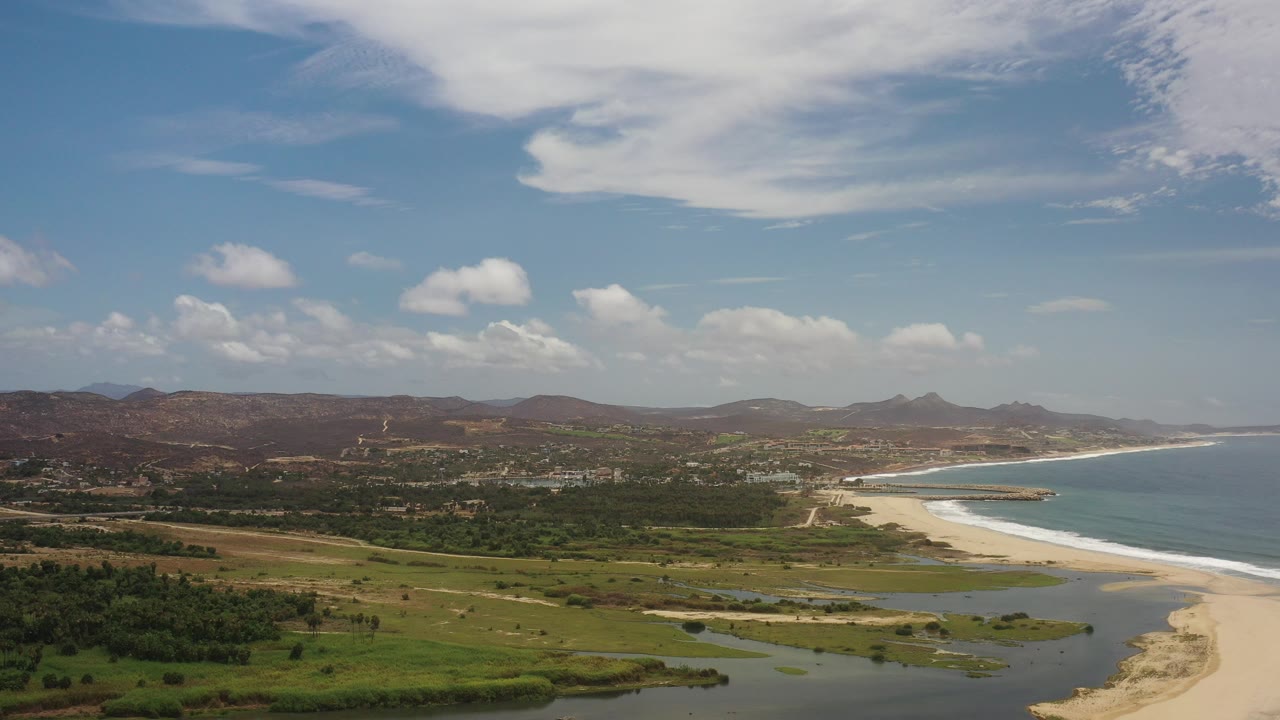 Wide coastal aerial view with beach, lagoon, ocean, hills, and blue sky.