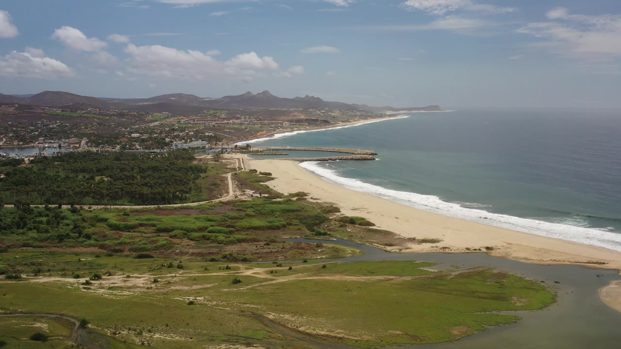 Aerial coastline with broad beach, ocean, foreground wetlands, town, and mountain ridge.