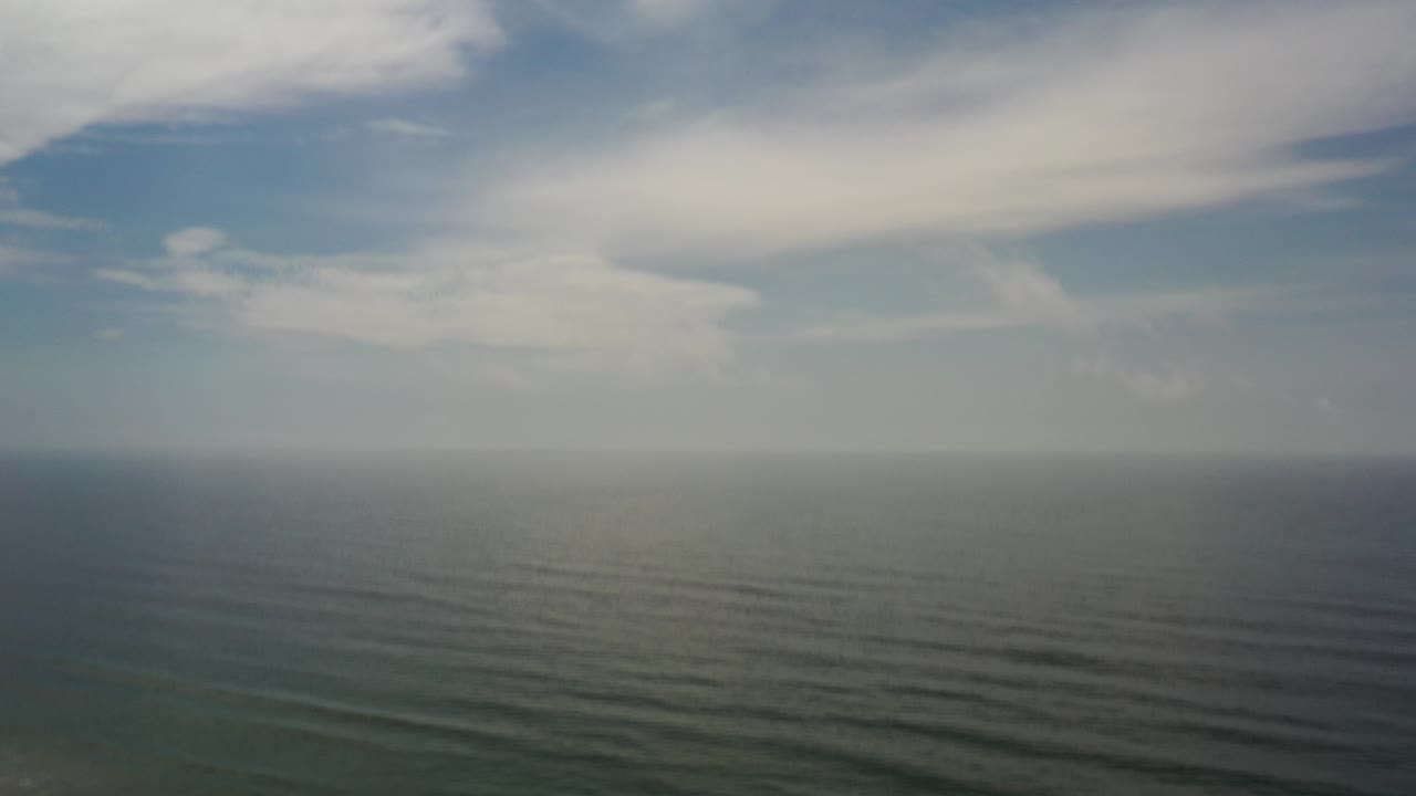 High aerial view over the ocean in Los Cabos, Mexico, with a hazy horizon, pale clouds, and no visible people.