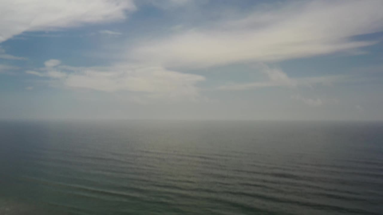 Aerial frame of green-gray ocean in Los Cabos, Mexico, with long parallel swell lines beneath a partly cloudy sky and no visible people.
