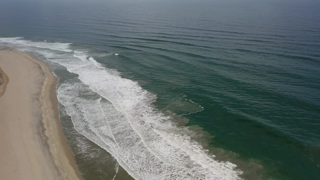 Aerial beach coastline with white surf over green water.