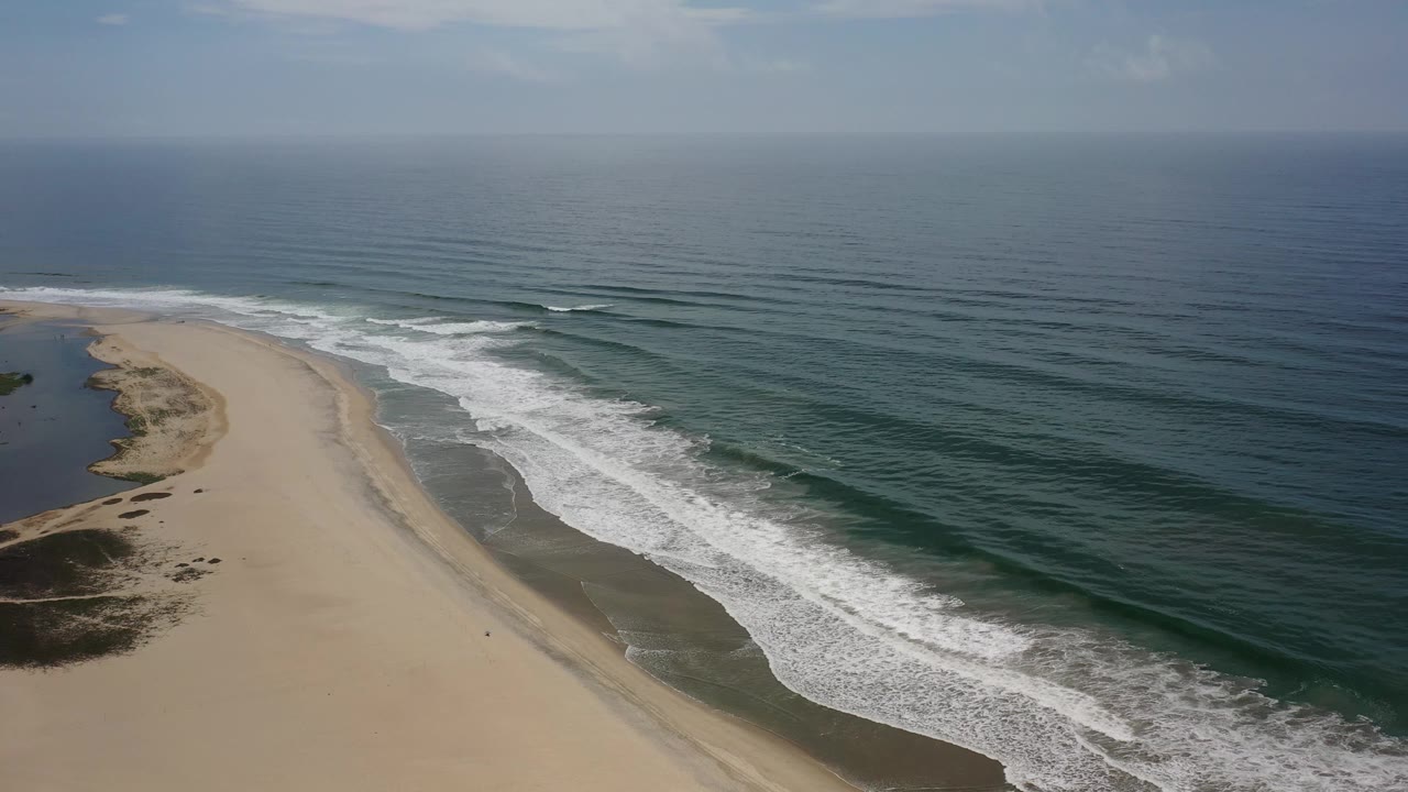 Curving beach beside dark ocean with white wave foam.