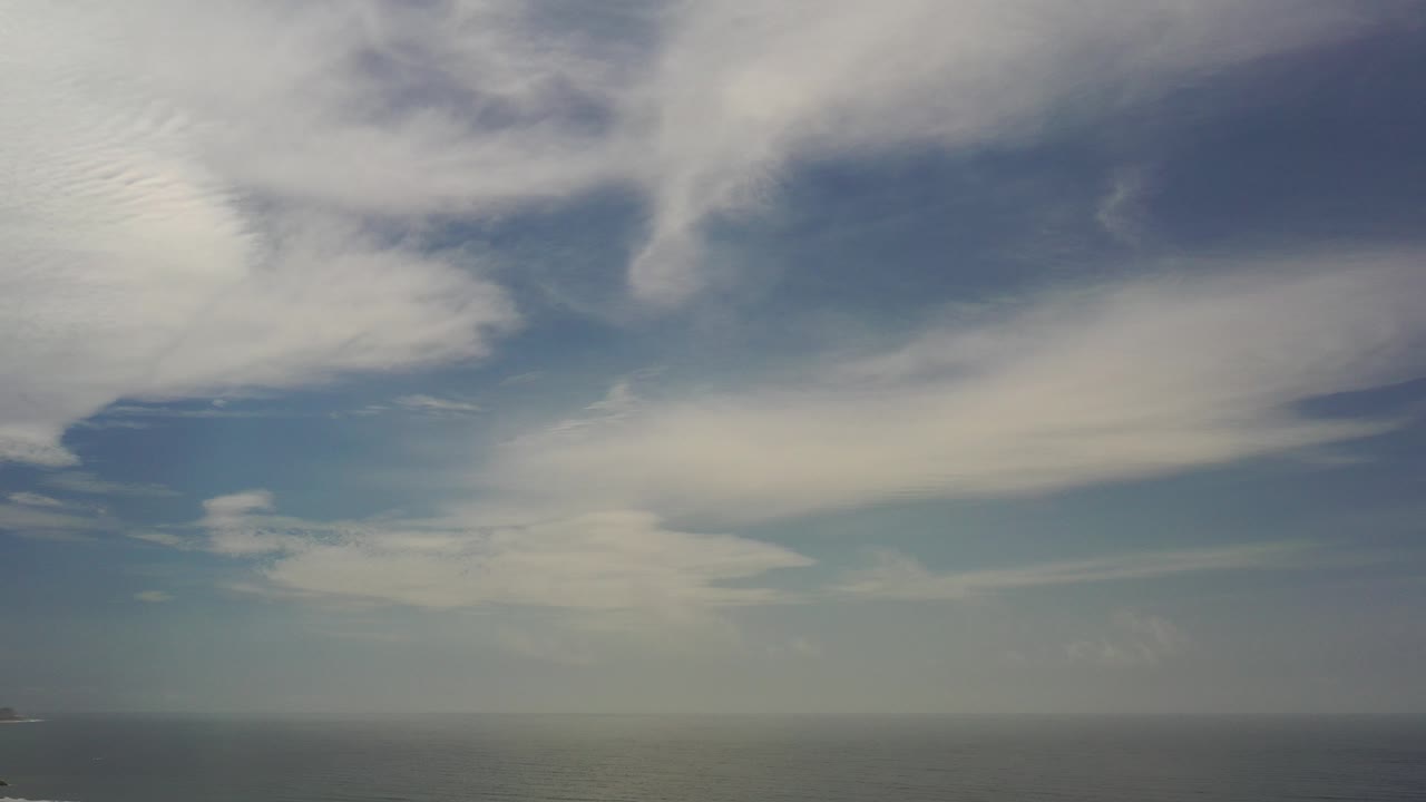Opening frame of a Los Cabos blue sky with layered white clouds, a thin hazy horizon near the bottom, and no visible people.
