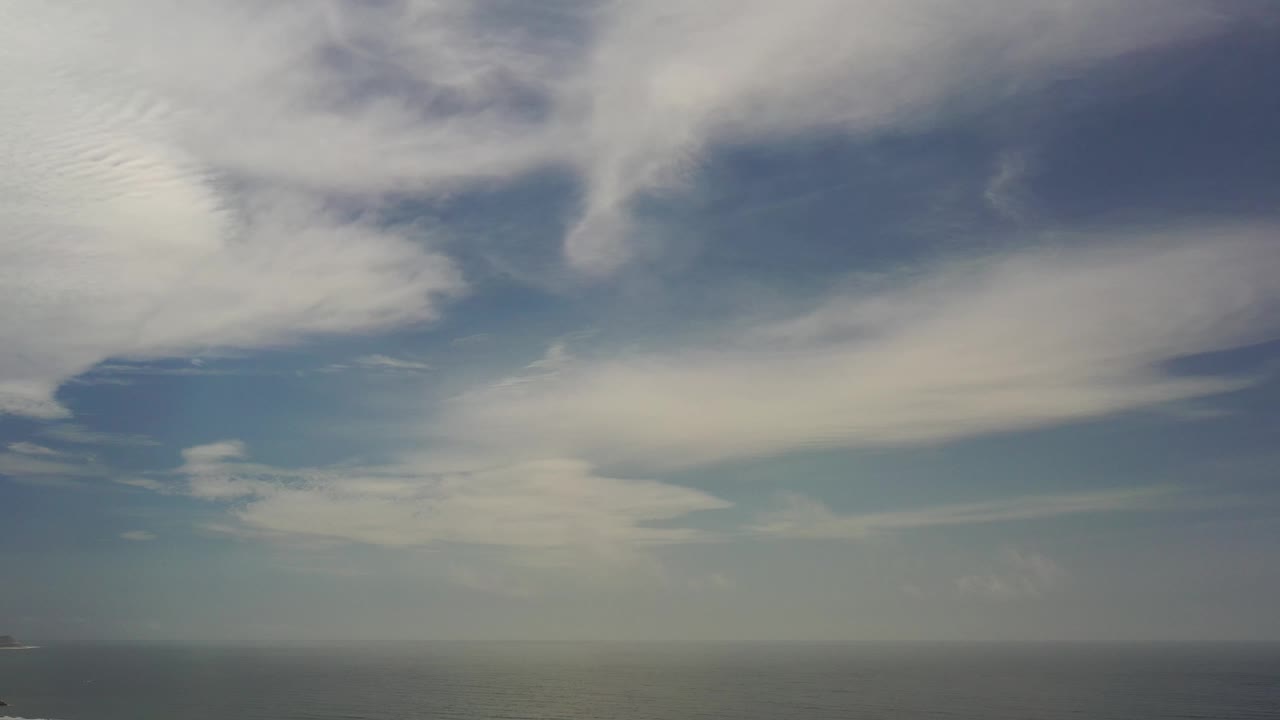 Los Cabos sky view at 0:01 with broad white cloud streaks across blue sky, muted haze near the horizon, and no visible people.