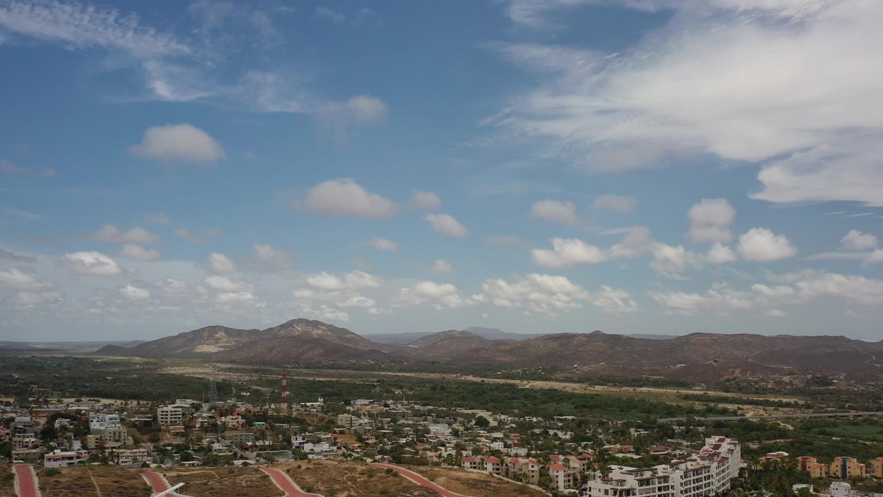 Aerial view of houses, roads, dry hills, and clouds.