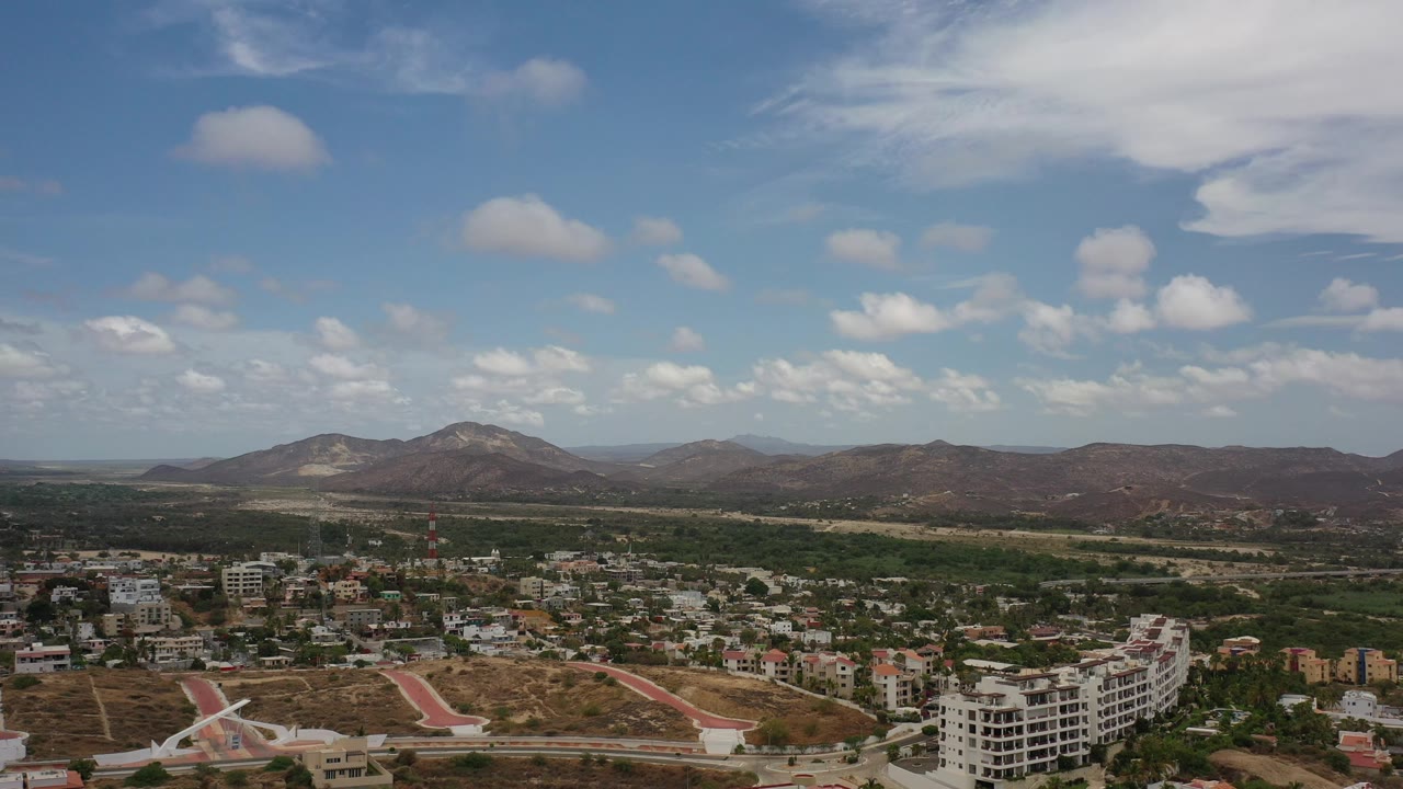 Town and hotel-like buildings beneath dry hills and scattered clouds.