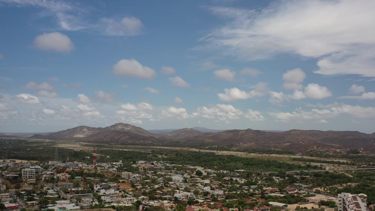 Wide sky over mountains with town buildings and trees below.