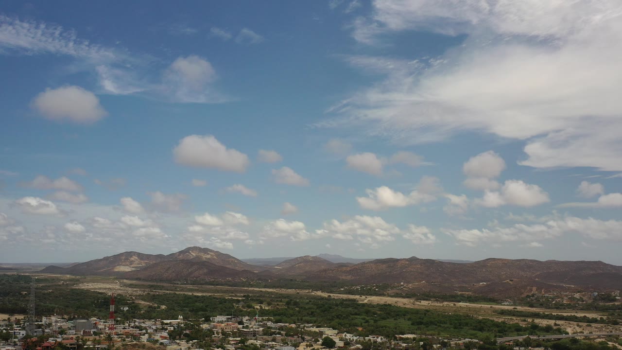 Wide view of mountains, scrubland, town edge, and blue sky with clouds.
